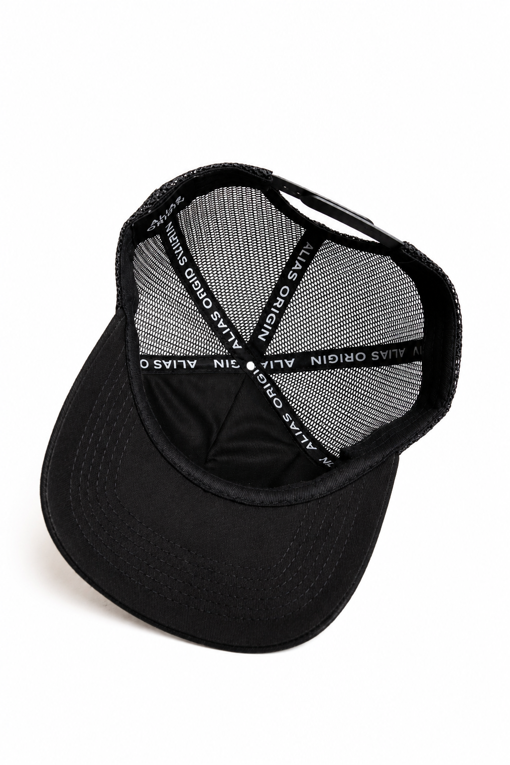 A black trucker hat with a black mesh back, showing an interior view from an angled top-down view on a white background. The interior view shows ALIAS ORIGIN branded taping with white text