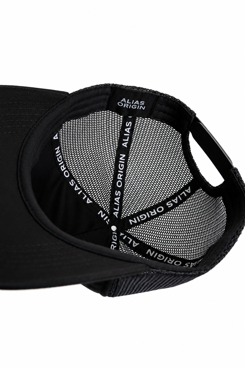 Close-up interior shot of a black trucker hat showing the mesh back with an adjustable strap with ALIAS ORIGIN interior branded taping with white text
